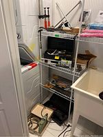 Overview of shelving unit holding various hand tools, a black tool case, nail box, clamps, and a mallet near a laundry setup.