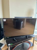 Frontal view of Toshiba 49in TV powered off, sitting on a black TV stand.
