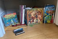 Wide photo showing educational toy set, children's books, puzzle, balloon pack and musical instruments including harmonica and wooden sticks