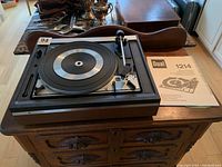 Full view of the Dual 1214 turntable on a wooden dresser alongside the instruction manual. Shows overall condition and missing lid.