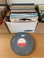 Box of assorted vinyl records, visible album covers, stored vertically in a cardboard Banker Box.