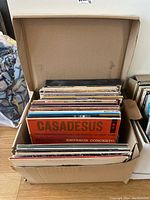 Box of assorted vinyl records, several albums visible with colorful covers and visible titles