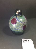 Front and side views of signed art glass bottle showing abstract decorative organic pattern in green, purple, and blue with spherical stopper.