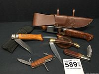 Group of five knives on black background, showing fixed blade, canvas sheath, brass-handled folder, multi-tool and Camillus folder