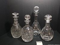 Four vintage crystal decanters arranged side by side with stoppers, varying in height and pattern. Clear detail of cut and etched glass surfaces.