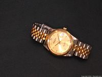 Angle of men's Dufonte watch face showing gold dial with diamond chip at 12 and two-tone band