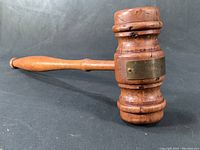 Side view of wooden gavel showing turned handle and brass plaque on the head.