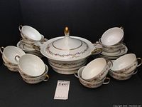26-piece Raynaud & Co Limoges Vieux Venise consumme set including lidded 2-handled tureen, stacked two-handled soup bowls, and saucers arranged on black background.