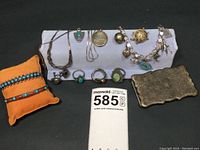 Wide view of all 13 jewelry pieces laid out including bracelets, rings, necklaces, belt buckle, and pin on black background