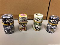 Front view of all four ceramic jars showing designs and gold hinged lids.