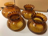 Four amber glass lamp shades with hobnail design and ruffled edges, three smaller and one larger.