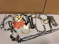 Photo of assorted jewelry mainly necklaces and some bracelets laid out on white surface showing variety of designs, colors, and materials