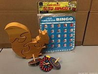 Photo showing a vintage Highway Auto Bingo game board, wooden 3D squirrel puzzle, and four colorful wooden spinning tops.