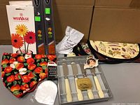 Full layout of assorted kitchen utensils and accessories showing multiple items including microplanes, cheese spreaders, bun warmers, floral arrangers, pot scraper, measuring spoon, and small grater.