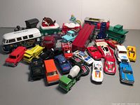 Top view showing 21 assorted toy cars and trucks including McDonald's Happy Meal train and Cars movie tow truck along with various diecast vehicles on a white surface.