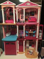 Front view of three-level pink Barbie Dreamhouse with visible bedroom, living room, kitchen, bathroom, and garage.