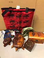 Image showing the red tote bag with black moose prints in the back, three fabric zippered pouches in front including a green crane pattern pouch and other colorful ones, two carved wooden turtles, and two wooden boxes with carved designs and metal clasps.