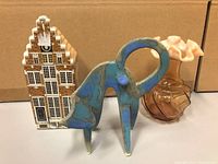 Dutch house ceramic figurine, abstract ceramic elephant, and amber glass vase shown together from front view.