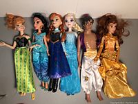 Six Disney character dolls side by side on a white background, including two Annas, Jasmine, Elsa, Aladdin, and Belle.