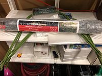 Full view of hardware mesh roll with red PEAK Fencing label and two greenhouse kits behind alongside green framing poles.