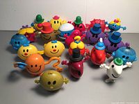 Front view of 20 colorful Mr. Men and Little Miss plastic figurines arranged closely together, displaying various characters with hats and smiling faces.