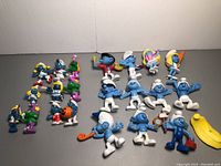 All 21 Smurf figurines and yellow accessory arranged on flat surface showing characters and colors