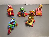 Five vintage plastic Muppet Babies toys from McDonald's on various wheeled ride-ons, including Animal, Kermit, Miss Piggy, Gonzo, and Fozzie Bear.