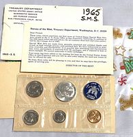 Original sealed plastic set containing five coins and a blue token with a turtle emblem, on top of a 1965 United States Assay Office envelope and information card.