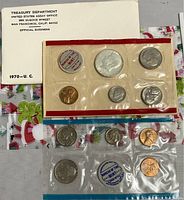 Two sealed 1970 US coin mint sets in plastic with titled envelopes and holiday gift bag underneath.