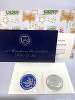 The entire lot showing the titled Department of the Treasury envelope with the coin description card and the sealed coin with a blank cardboard protection piece, all with a holiday gift bag partially visible behind.