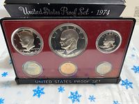 1974-S US coin proof set displayed with six proof coins inside plastic holder, on snowflake-patterned cloth, with titled black box.
