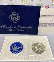 Photo of the blue titled envelope with Department of the Treasury seal and the sealed coin and blue sticker side by side.
