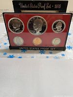 Front view of the 1976 US Bicentennial proof coin set in plastic display case with red background and black base, showing six coins in place.