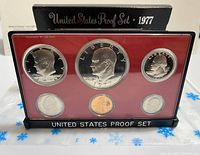 Front view of the 1977-S United States Proof Set coins in clear plastic case on red background with black base and titled box with 'United States Proof Set 1977' text.