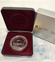 Front view of open burgundy velvet-lined box showing encapsulated silver coin inside with silver-colored outer cardboard sleeve to the side, featuring Royal Canadian Mint logo and text.