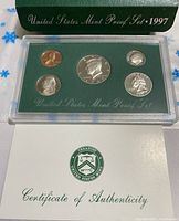 Photo showing the five 1997-S proof coins in a clear plastic case with green insert labeled 'United States Mint Proof Set 1997'. Certificate of Authenticity partially visible underneath.