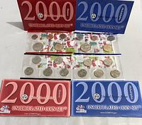 Two sealed 2000 United States Mint uncirculated coin sets with red and blue envelopes, displayed with coins and plastic sleeves visible.
