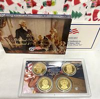 Set displayed in original plastic casing, showing four $1 coins, themed background card, and outer box with holiday gift bag.