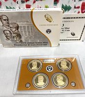 Photo of the cardboard box and plastic case with the four proof coins visible, along with the Certificate of Authenticity behind the box.