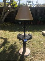 Full view of the 1980s freestanding lamp with beige fabric lampshade and wooden base on a grassy outdoor surface.