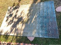 Blue green area rug placed on grass, showing gradient colors and texture. Shadow patterns partially cover the surface.
