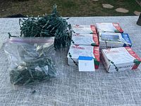 Six boxes of Christmas lights mostly 100 light sets and some loose strings of unused lights in a plastic bag.
