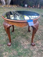 Full view of round glass mirrored coffee table set outdoors on grass, showing claw feet and burlwood accent.
