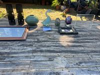 Wide view of all items on wooden table outdoors including vase, goose figurine, candle holders, picture frames, and paperweight.