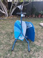 Full view of the collapsible bike stand displaying the tripod legs, the clamp on the top, and the two boogie boards positioned behind it on grass.