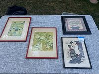 Four framed Asian art prints displayed on a grey fabric surface outdoors, showing overall lot.