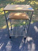 Full view of metal rolling kitchen cart with wooden top and wire shelves, showing wooden cutting board on middle shelf.