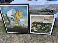Two Salvador Dali posters outdoors showing size difference and condition; wood frames with visible water damage.