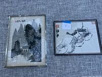 Both framed signed Asian art prints displayed on grey fabric surface