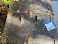 Closed top view showing the heavily worn, black travel chest with metal reinforcements and rusted lock.